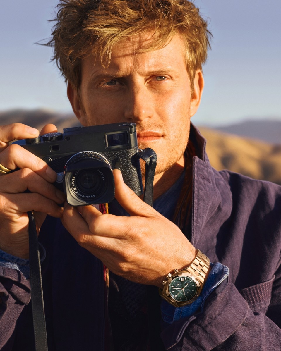 Uomo che tiene una macchina fotografica in un paesaggio desertico con le montagne sullo sfondo.