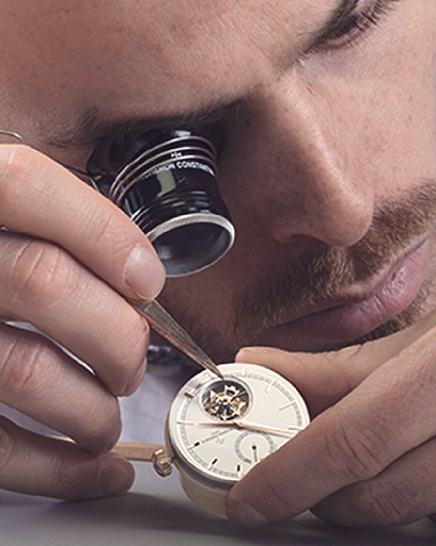 Watchmaker inspecting a mechanical movement through a loupe while adjusting it with a tool.