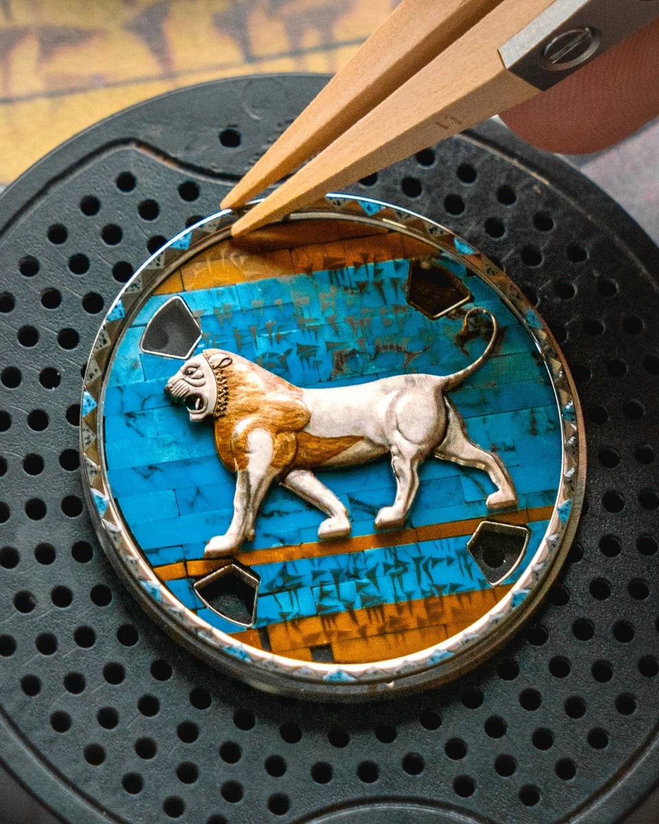 Pinzette che posizionano un quadrante smaltato con un disegno di leone su un supporto per orologi.