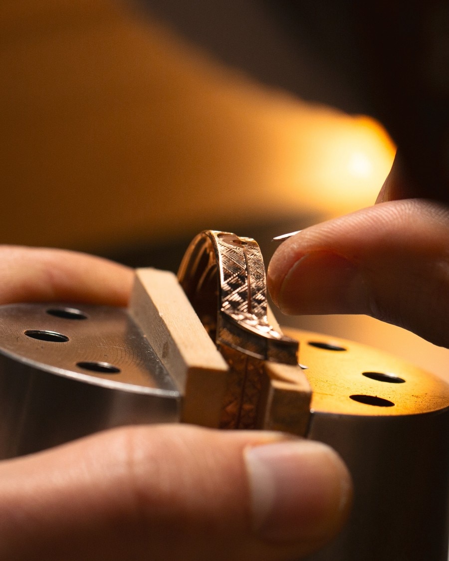 Artisan holding and working on an engraved watch component under warm lighting.