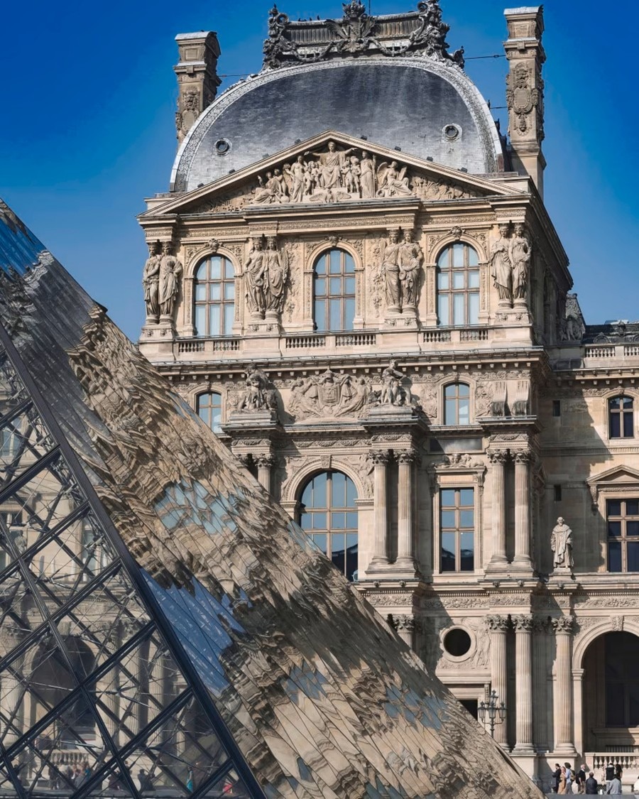 Storico edificio del Louvre a Parigi con la piramide di vetro in primo piano.