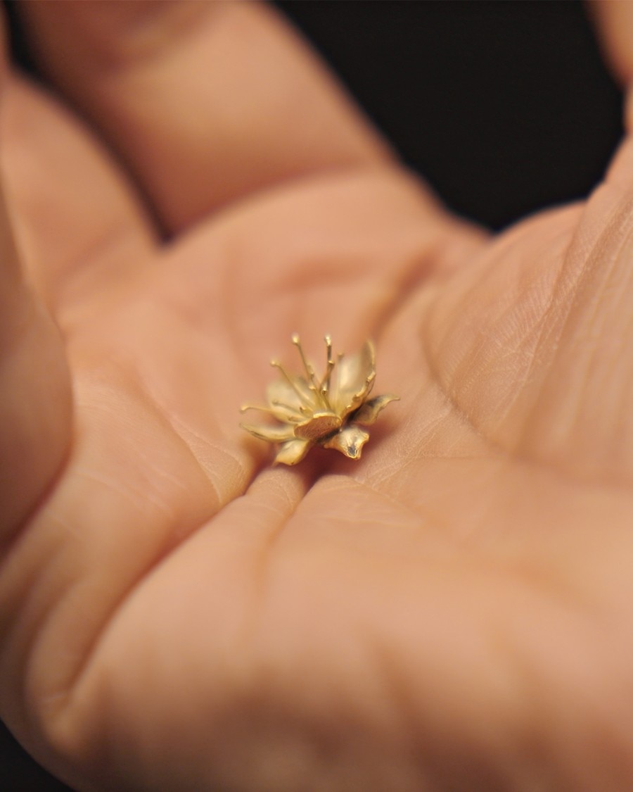 Un fiore in miniatura color oro appoggiato sul palmo di una mano.