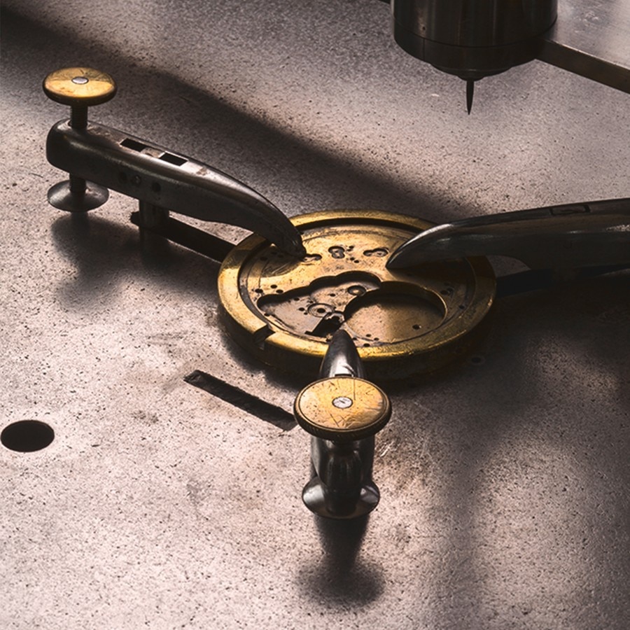 A golden watch movement is being worked on with tools.
