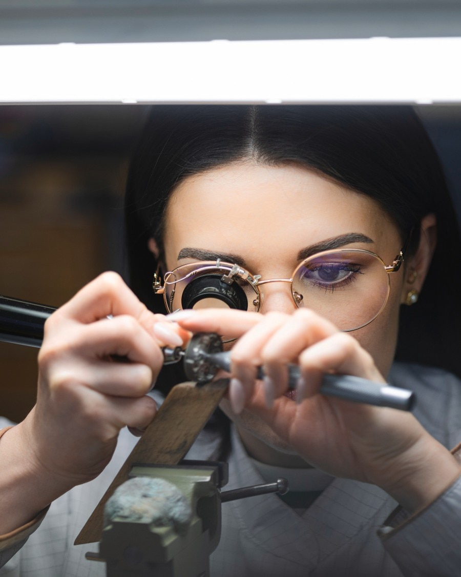 Craftswoman working on a fine watch component under magnification with a precision tool.
