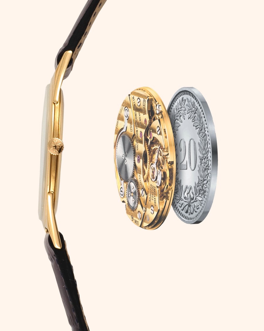 Side view of an ultra-thin wristwatch with a gold case and black strap, showcasing its thin profile next to two coins for comparison.