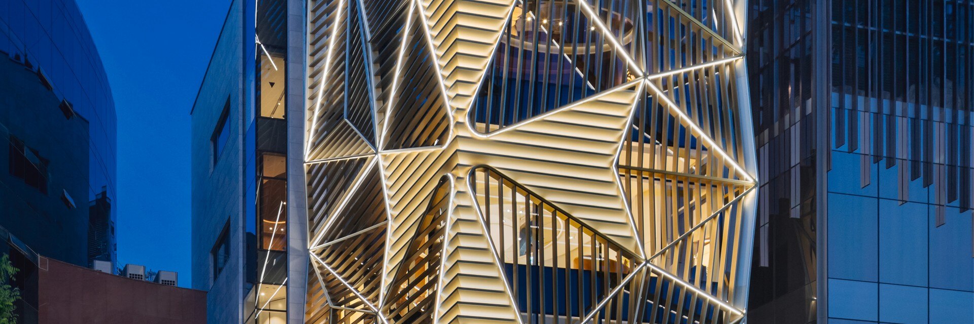 A modern building with a brightly lit geometric facade and a Maltese cross.