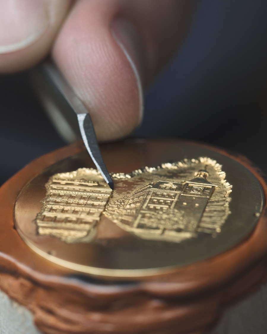 Close-up of engraving in progress, depiciting buildings on a round metal piece.