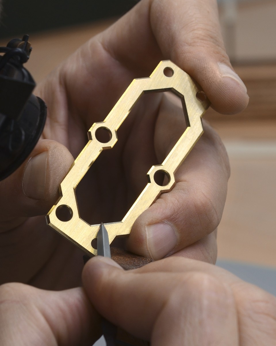Finitura manuale dei bordi di un componente di un orologio in oro.