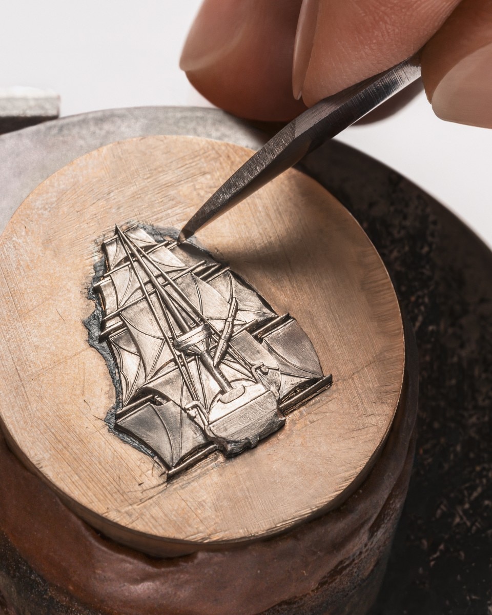 Close-up of engraving a ship motif on a round metal dial.