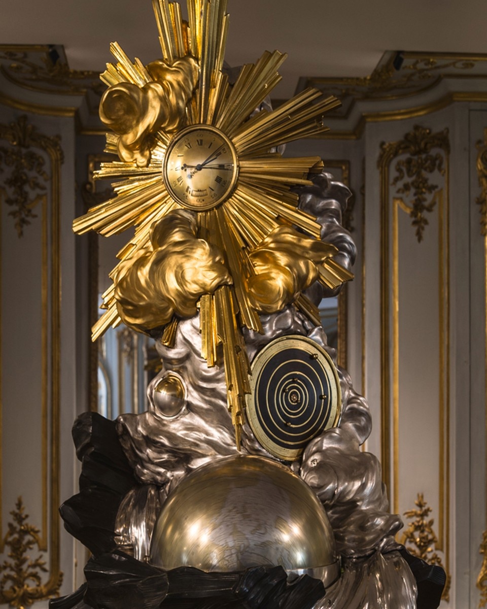 Ornate golden clock sculpture with sun-shaped rays in a baroque interior.