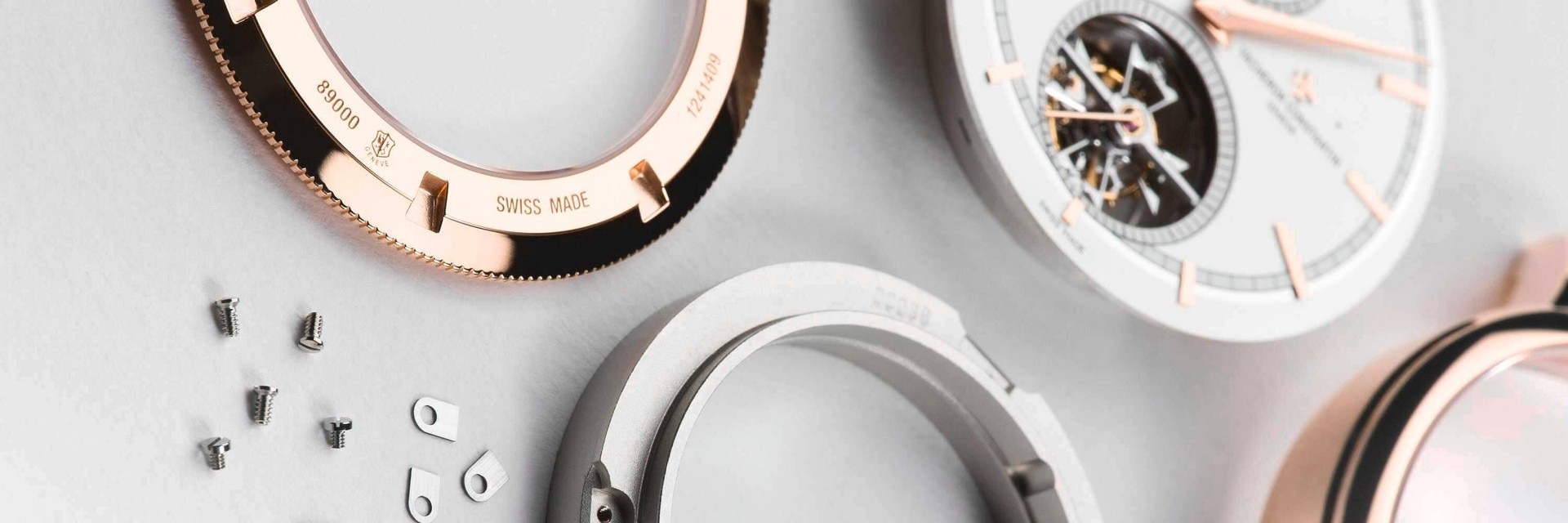 Un assortiment de composants de montres Vacheron Constantin, y compris des boîtiers, des mouvements et des engrenages, exposés sur une surface claire.