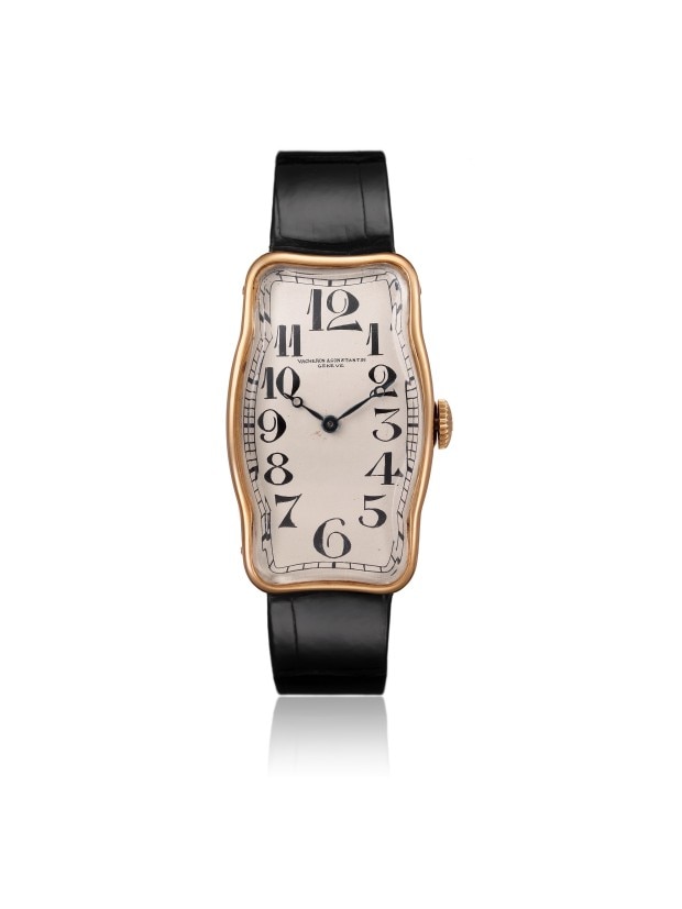 A gold wirstwatch with a distinctive wavy rectangular case, black numerals, and a black leather strap.