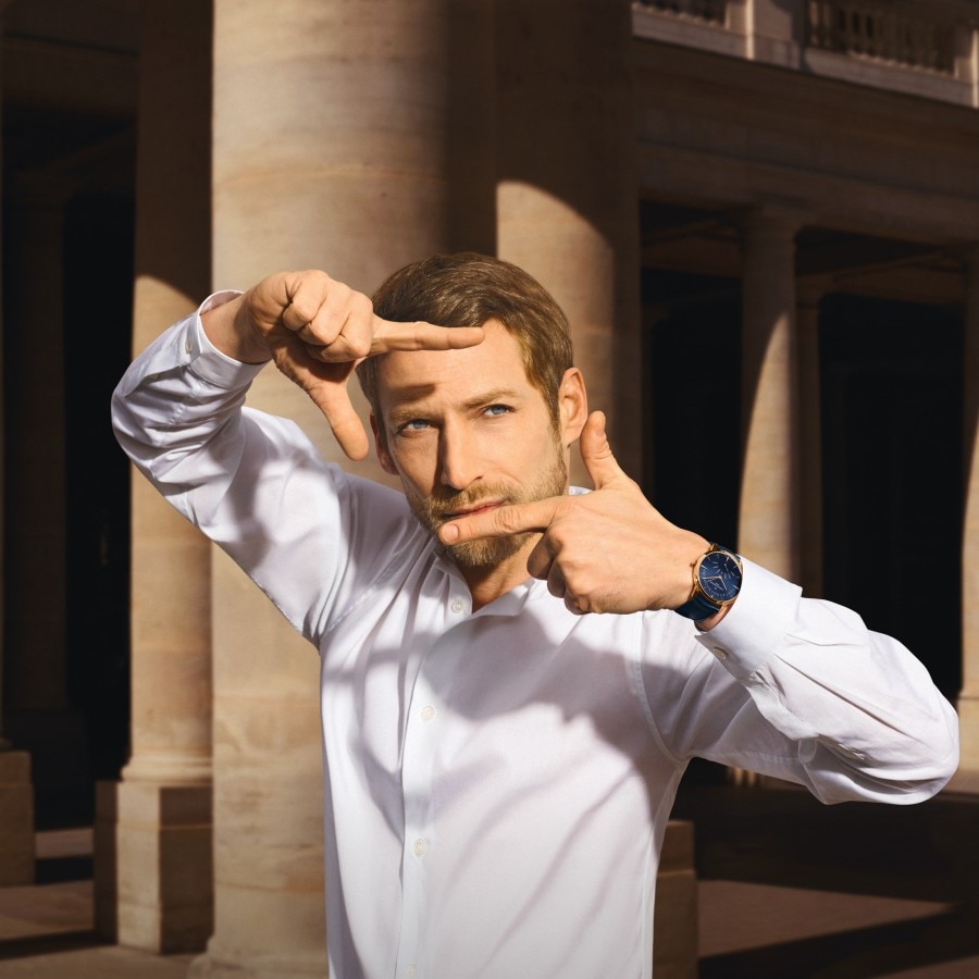 Man in white shirt framing with hands, wearing a dress watch with white dial and brown strap.