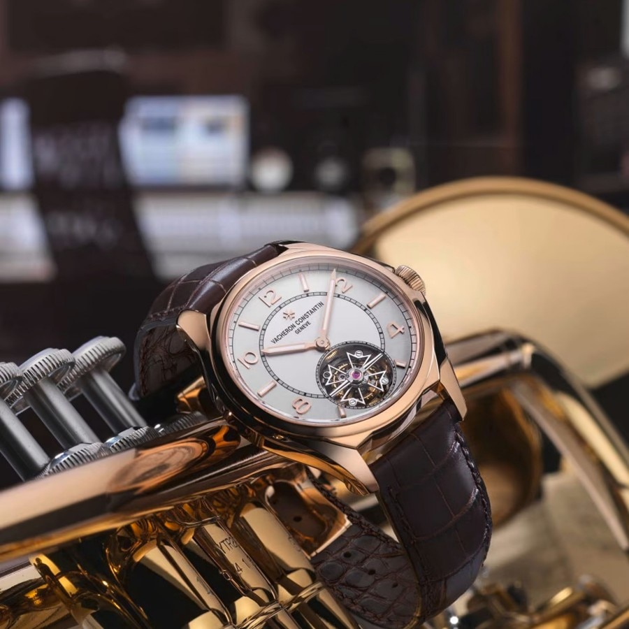 A luxury watch with a brown leather strap placed on a golden trumpet.