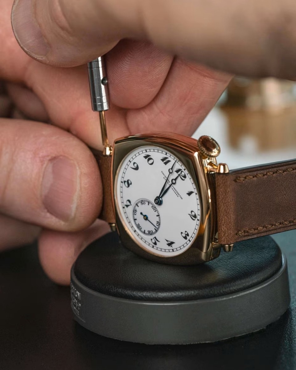 A hands working on a watch with a gold frame and brown leather strap