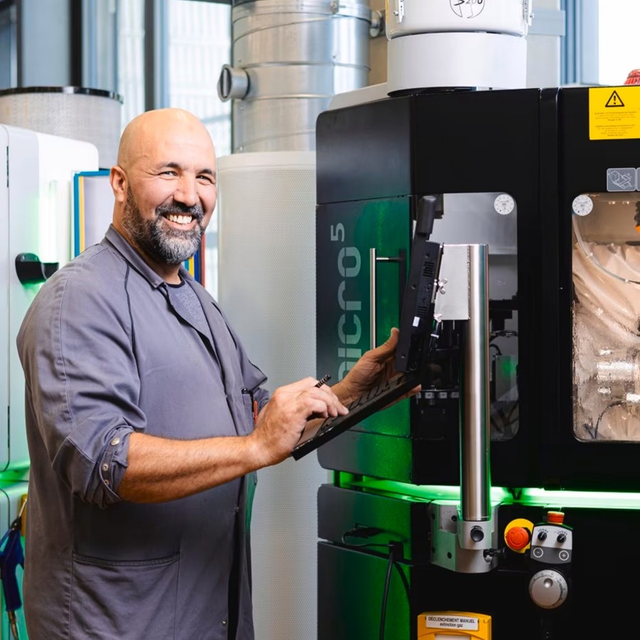 Smiling technician operating a green industrial machine in a modern workshop environment.