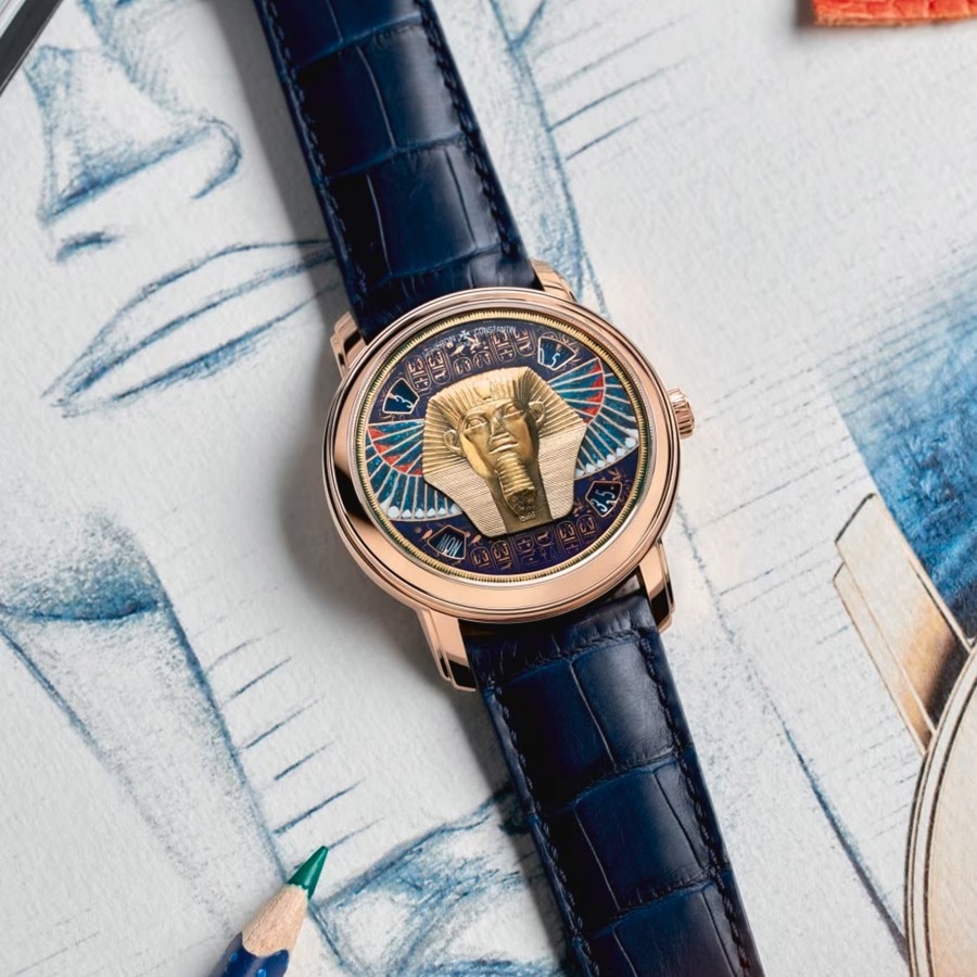 Luxury watch with a blue strap and a dial featuring a sculpted gold ram's head against a colorful background.